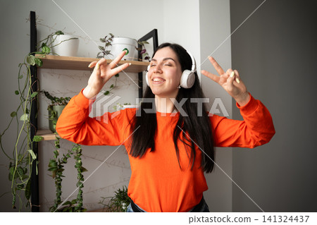 Young woman enjoying music with wireless headphones in a brightly lit room. Music streaming positive lifestyle and digital entertainment Young woman enjoying music with wireless headphones in a brightly lit room. Music streaming positive lifestyle and digital entertainment 141324437