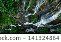 Aerial view of deep tropical rainforest with waterfall surrounded by lush tropical forest and towering cliffs streams of water into deep canyon, Lush green trees in forest with natural stream. 141324864