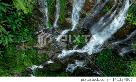 Aerial view of deep tropical rainforest with waterfall surrounded by lush tropical forest and towering cliffs streams of water into deep canyon, Lush green trees in forest with natural stream. Aerial view of deep tropical rainforest with waterfall surrounded by lush tropical forest and towering cliffs streams of water into deep canyon, Lush green trees in forest with natural stream. 141324865