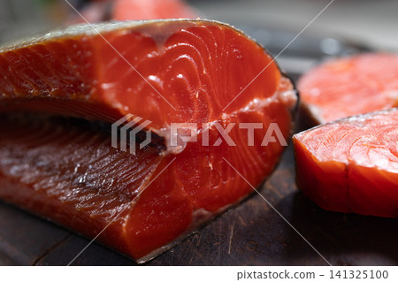 Closeup smoked sockeye salmon fillet with rich red flesh on rustic wooden board, sliced into thick portions for gourmet food presentation and detailed texture display Closeup smoked sockeye salmon fillet with rich red flesh on rustic wooden board, sliced into thick portions for gourmet food presentation and detailed texture display 141325100