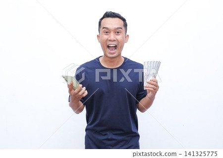 Man smiles joyfully while holding cash and phone. He appears delighted, possibly celebrating earnings or success. Pure white background ensures focus on his expression and objects Man smiles joyfully while holding cash and phone. He appears delighted, possibly celebrating earnings or success. Pure white background ensures focus on his expression and objects 141325775