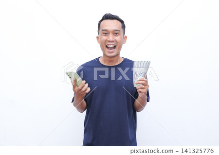 Man smiles joyfully while holding cash and phone. He appears delighted, possibly celebrating earnings or success. Pure white background ensures focus on his expression and objects Man smiles joyfully while holding cash and phone. He appears delighted, possibly celebrating earnings or success. Pure white background ensures focus on his expression and objects 141325776