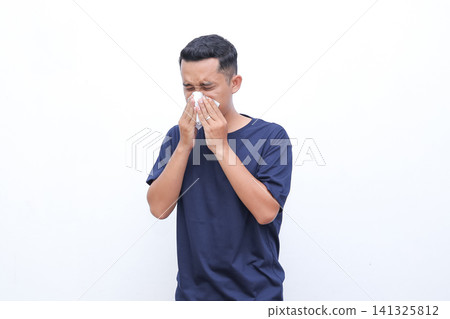 Man wipes nose with tissue. He looks distressed or ill. Simple background highlights his action. Perfect for allergy or flu related content. Use in health, wellness, or medical contexts Man wipes nose with tissue. He looks distressed or ill. Simple background highlights his action. Perfect for allergy or flu related content. Use in health, wellness, or medical contexts 141325812