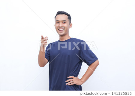 Young man smiles brightly, thumbs up. He wears a simple navy tshirt. One hand rests on his hip, the other gestures. Background is clean, white, distraction free Young man smiles brightly, thumbs up. He wears a simple navy tshirt. One hand rests on his hip, the other gestures. Background is clean, white, distraction free 141325835
