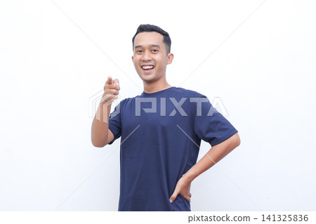 Young man smiles brightly, thumbs up. He wears a simple navy tshirt. One hand rests on his hip, the other gestures. Background is clean, white, distraction free 141325836