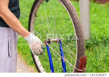 Man fixing bicycle wheel at doorstep. Own vehicle maintenance without service center. Responsible ownership visible. Summer commute switched to pedal power Man fixing bicycle wheel at doorstep. Own vehicle maintenance without service center. Responsible ownership visible. Summer commute switched to pedal power 141326267
