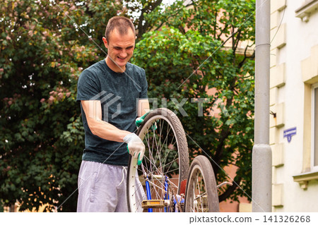 Young man repairing bike chain on sidewalk. Quick fix before summer rides. Responsible transport care and preparation for summer season Young man repairing bike chain on sidewalk. Quick fix before summer rides. Responsible transport care and preparation for summer season 141326268