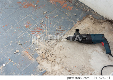 A powerful hammer drill with an orange glove rests on a concrete floor covered in debris 141326281