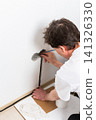 Worker runs new electrical wires into a cutout in a white apartment wall. This task prepares for the installation of an electrical outlet near the baseboard 141326330