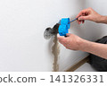Skilled electrician carefully places blue flush-mount boxes into a wall opening, preparing for a new double electrical outlet installation in an apartment during home improvement 141326331