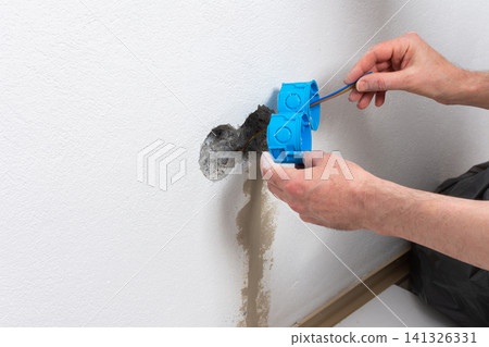 Skilled electrician carefully places blue flush-mount boxes into a wall opening, preparing for a new double electrical outlet installation in an apartment during home improvement Skilled electrician carefully places blue flush-mount boxes into a wall opening, preparing for a new double electrical outlet installation in an apartment during home improvement 141326331