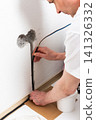 Worker runs new electrical wires into a cutout in a white apartment wall. This task prepares for the installation of an electrical outlet near the baseboard 141326332