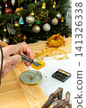 A man is using a tool to fix the wiring of a Christmas tree garland. Tools are spread out on the table as he works carefully in a room decorated for the holidays 141326338