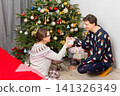 On Christmas Day, a 52-year-old couple spends time together near a decorated tree. They exchange gifts and celebrate the holiday in their cozy home setting filled with decorations 141326349