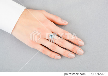 Beautiful female hand with gold ring with diamonds and aquamarine on gray background 141326563