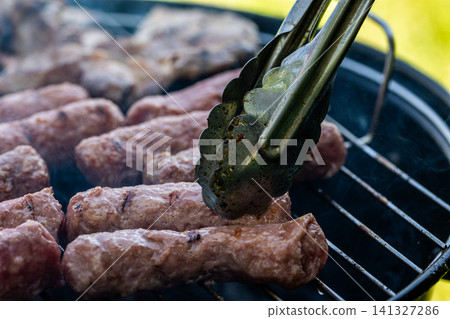 Close-up of roasted cevapi, cevapcici on the grill over glowing charcoal, traditional Balkan meat sausages on the bbq Close-up of roasted cevapi, cevapcici on the grill over glowing charcoal, traditional Balkan meat sausages on the bbq 141327286