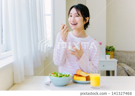 A young woman eating yogurt for breakfast 141327468