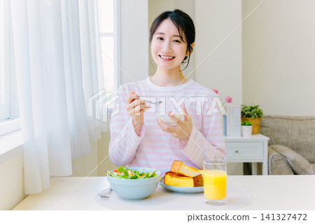 A young woman eating yogurt for breakfast A young woman eating yogurt for breakfast 141327472