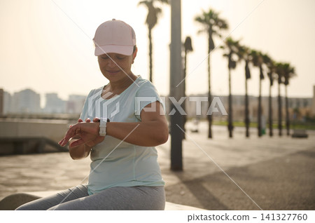 Woman checking smartwatch after outdoor exercise on a palm-lined city promenade Woman checking smartwatch after outdoor exercise on a palm-lined city promenade 141327760