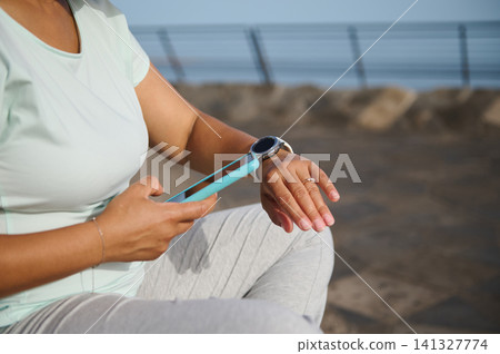 Woman checking smartwatch while holding smartphone after outdoor workout 141327774
