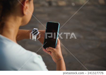 Woman checking smartwatch with smartphone in hand after outdoor workout wearable fitness technology Woman checking smartwatch with smartphone in hand after outdoor workout wearable fitness technology 141327776