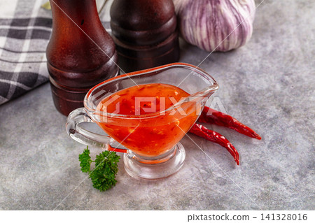 Spicy chili sauce in glass gravy boat with dried peppers and garlic Spicy chili sauce in glass gravy boat with dried peppers and garlic 141328016