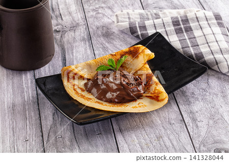 Folded crepe with chocolate spread and mint on black plate Folded crepe with chocolate spread and mint on black plate 141328044
