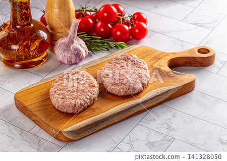 Raw burger patties on wooden cutting board with fresh ingredients Raw burger patties on wooden cutting board with fresh ingredients 141328050