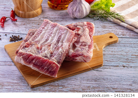 Fresh raw pork ribs with garlic, rosemary and chili pepper on a wooden kitchen board Fresh raw pork ribs with garlic, rosemary and chili pepper on a wooden kitchen board 141328134