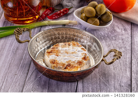 Baked camembert cheese in hammered metal dish with olives and chili peppers Baked camembert cheese in hammered metal dish with olives and chili peppers 141328160