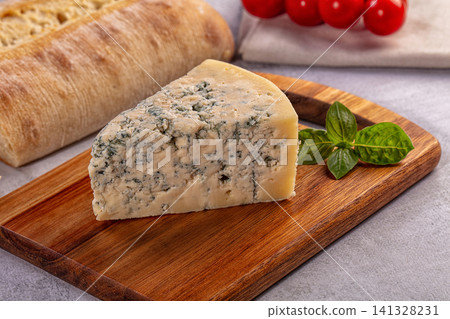 Blue cheese wedge on wooden board with basil and bread Blue cheese wedge on wooden board with basil and bread 141328231