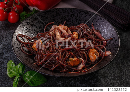 Black spaghetti with squid and mussels on dark plate with basil and cherry tomatoes Black spaghetti with squid and mussels on dark plate with basil and cherry tomatoes 141328252