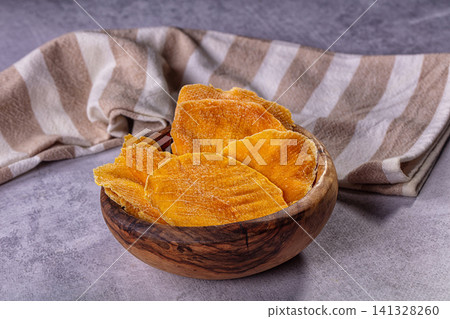 Dried mango slices in wooden bowl on striped cloth Dried mango slices in wooden bowl on striped cloth 141328260
