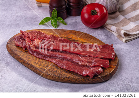 Raw beef steak slices on wooden cutting board with tomato basil garlic Raw beef steak slices on wooden cutting board with tomato basil garlic 141328261