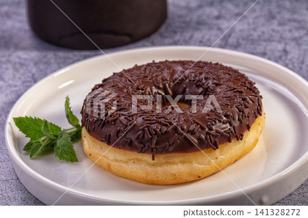 Chocolate frosted donut with sprinkles on white plate with mint garnish Chocolate frosted donut with sprinkles on white plate with mint garnish 141328272