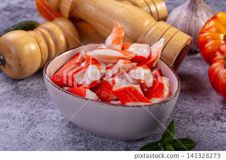 Bowl of surimi crab sticks with wooden pepper mill and fresh vegetables on gray stone surface Bowl of surimi crab sticks with wooden pepper mill and fresh vegetables on gray stone surface 141328273