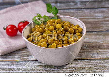Bowl of canned peas with cherry tomatoes and pea sprigs on rustic wood 141328285