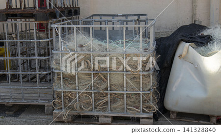Fishing nets and tangled ropes are piled inside a metal crate in a rustic industrial port harbor. The area shows signs of daily fishing activity. Fishing nets and tangled ropes are piled inside a metal crate in a rustic industrial port harbor. The area shows signs of daily fishing activity. 141328840