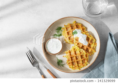 Vegetarian potato waffles with natural yogurt and dill on a plate on a light background with shadows 141329099