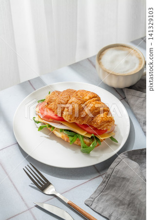 A golden croissant sandwich with ham, cheese, tomato, and arugula on a tile background A golden croissant sandwich with ham, cheese, tomato, and arugula on a tile background 141329103
