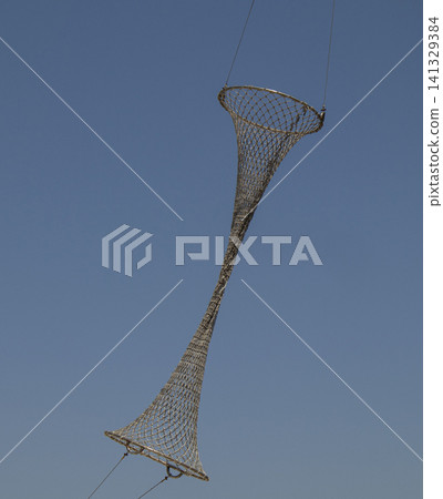 A metal ring fishing net is suspended high against a clear blue sky. This setup is common in traditional fishing practices found near coastal regions. A metal ring fishing net is suspended high against a clear blue sky. This setup is common in traditional fishing practices found near coastal regions. 141329384