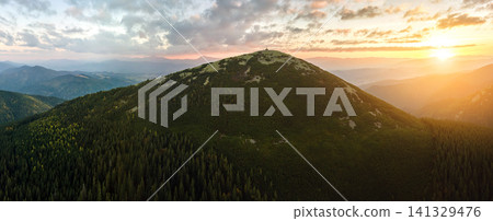 Aerial view of amazing scenery with foggy dark mountain peak covered with forest pine trees at autumn sunrise. Beautiful wild woodland with shining rays of light at dawn Aerial view of amazing scenery with foggy dark mountain peak covered with forest pine trees at autumn sunrise. Beautiful wild woodland with shining rays of light at dawn 141329476