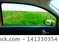 A view of the green embankment and the side mirror from the passenger seat. 141330354