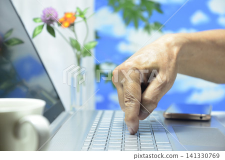 A close-up of a laptop computer and an elderly person's hand. A close-up of a laptop computer and an elderly person's hand. 141330769