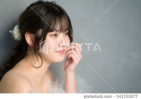 A Japanese woman in a wedding dress smiles, resting her chin on her hand against a gray background. A Japanese woman in a wedding dress smiles, resting her chin on her hand against a gray background. 141332677