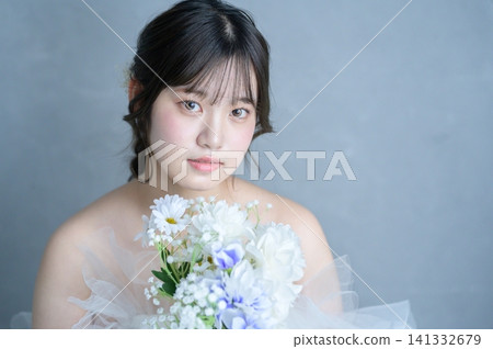 一位身穿婚紗的日本女子手捧花束,在灰色背景下凝視著遠方。 一位身穿婚紗的日本女子手捧花束,在灰色背景下凝視著遠方。 141332679