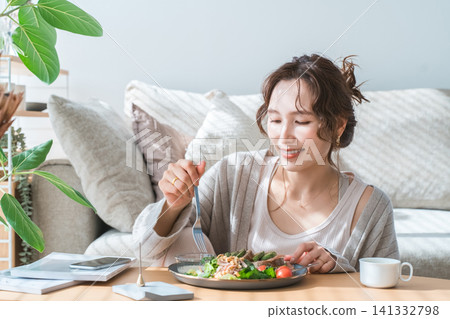 Stylish young Asian woman eating at the living room table Stylish young Asian woman eating at the living room table 141332798