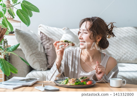 Stylish young Asian woman eating at the living room table Stylish young Asian woman eating at the living room table 141332800