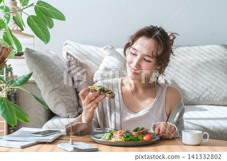Stylish young Asian woman eating at the living room table 141332802