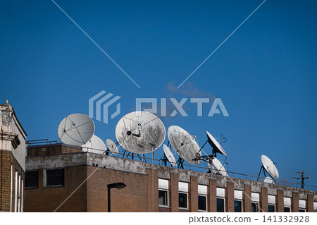 Parabolic antennas designed to receive or transmit radio wave information. They are mounted on a brick building under a clear blue sky 141332928